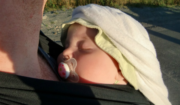Varför bära barn. Bebis sover i bärsjal, pappa på språng.