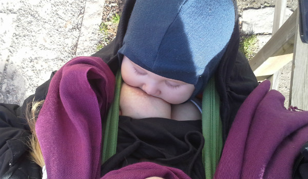 Bära en nyfödd bebis i bärsjal. Amning i bärsjal utomhus.
