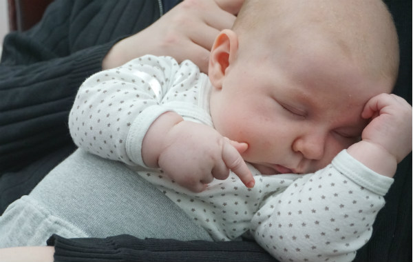 Socialstyrelsens sovråd för bebisar. Bebis sover i en vuxens famn.