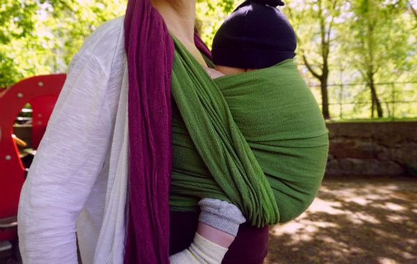 Bära en nyfödd bebis i bärsjal. Bebis sover i grön bärsjal, sommar.