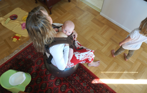 Bära en nyfödd bebis i bärsjal. Amning i bärsele på pilatesboll i vardagsrum.