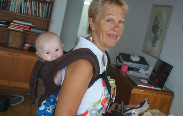 Bära en nyfödd bebis i bärsjal. Mormor med barnbarn i bärsele på ryggen.
