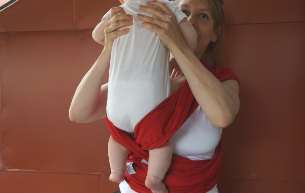 Bildserie: Amma i trikåsjal. Bebis dras upp ur röd bärsjal.