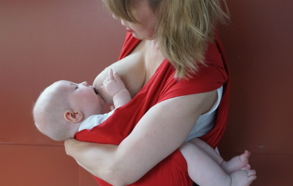 Bildserie: Amma i trikåsjal. Bebis ligger ned i röd bärsjal, greppar bröstet.