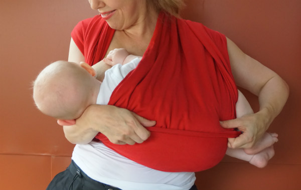 Bildserie: Amma i trikåsjal. Bebis ligger ned och ammar i röd bärsjal. Mamman drar upp ett extra lager tyg över barnets kropp.