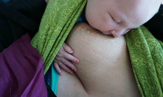 Nyfödd sväljer bröstmjölk. Bebis ammar i grön bärsjal.