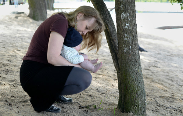 Amningsstrejk. Babypottning i det fria, mamma håller bebis i knävecken på en strand.