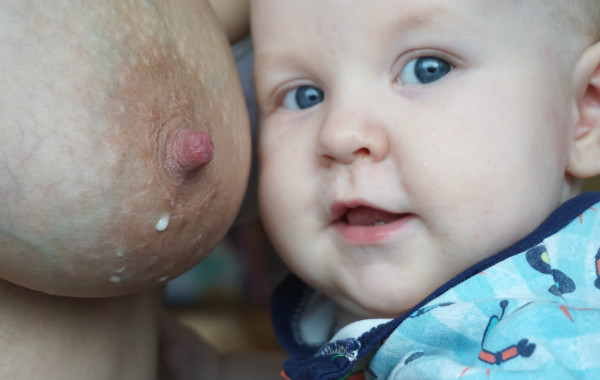 Amningsstrejk. Bröst med mjölkdroppe och leende bebis bredvid bröstet.