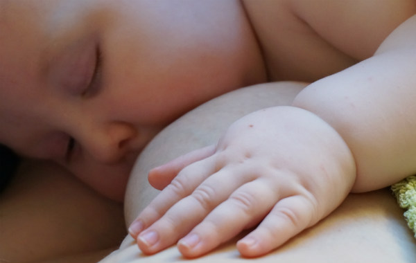 Amningsstrejk. Bebis ammar i sömnen, närbild. Liten hand på bröst.
