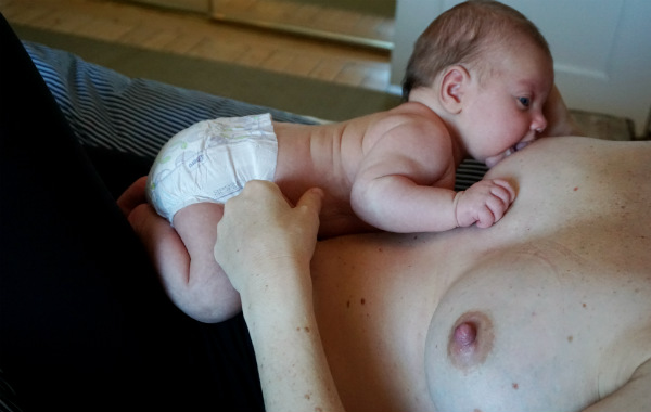 Magical hour, magiska timmen. Fem veckor gammal bebis på mammans bröst, säng. Bebisen söker bröstet, tillbakalutad amning.