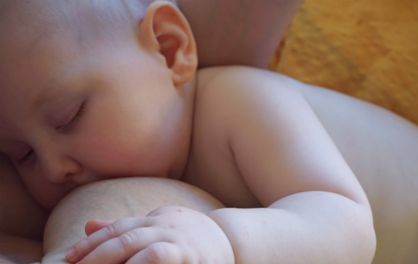När du snart ska börja amma. Liten bebis ammar och sover, har en hand på bröstet.