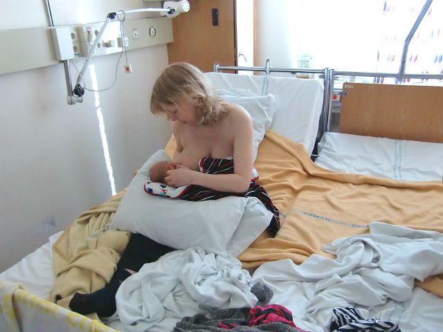 Empati och amningskunskap. Mamma ammar bebis på BB, sittande i säng.