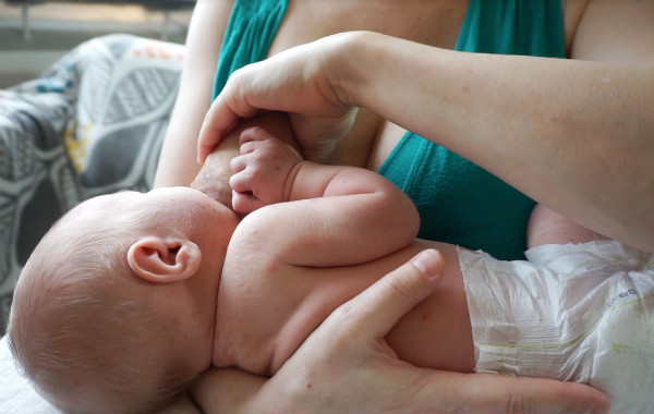 Bröstkompressioner. Hand klämmer om bröst vid amning av liten bebis.