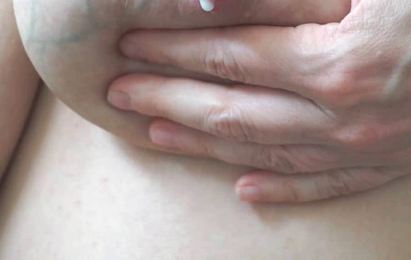 Handmjölkning. Hand runt bröst, mjölkdroppe kommer från bröst.