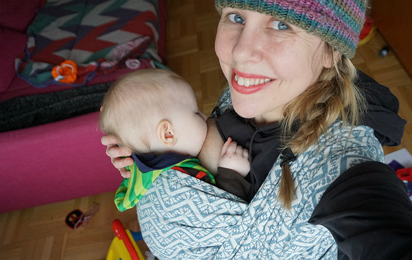 Empati och amningskunskap. Lisen Forsberg med ammande bebis i bärsjal, inomhus.