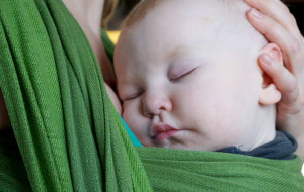 Empati och amningskunskap. Bebis har somnat i grön bärsjal, närbild.