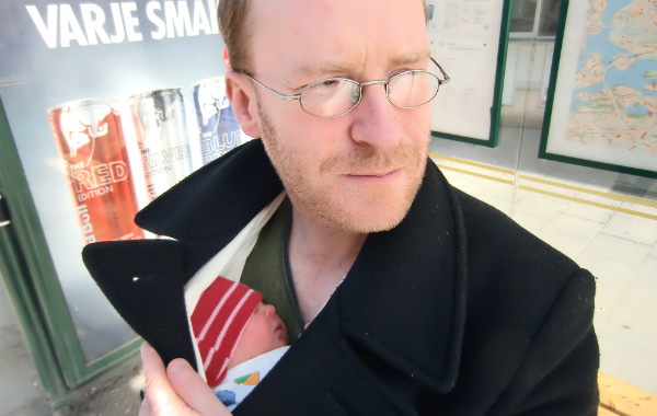 Bärsjal på BB. Pappa bär alldeles nyfödd bebis i bärsjal innan för rocken på busshållplats, stadsmiljö.