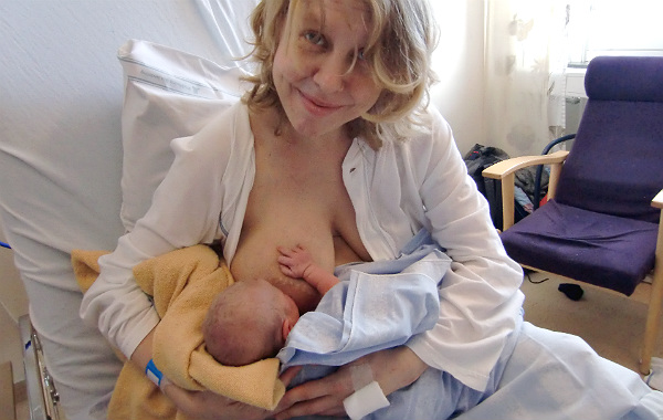 Empati och amningskunskap. Mamma ammar nyfödd bebis, sittande i säng på BB. Tittar in i kameran.