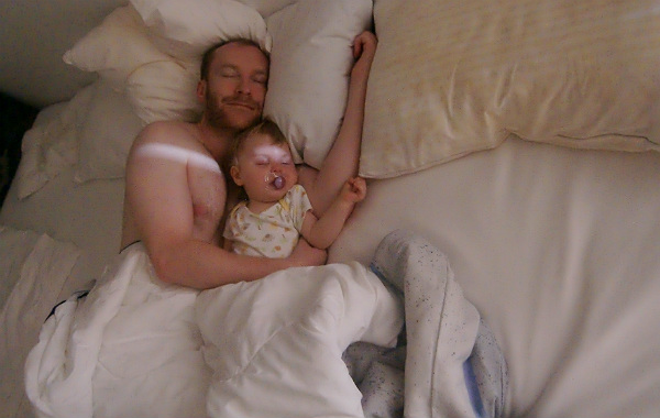 Personligt om samsovning. Ettåring sover på pappas arm i säng.
