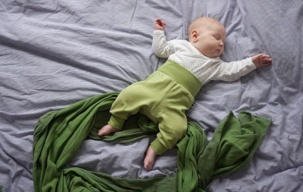 Personligt om samsovning. Bebis sover på säng, ovanpå grön bärsjal.