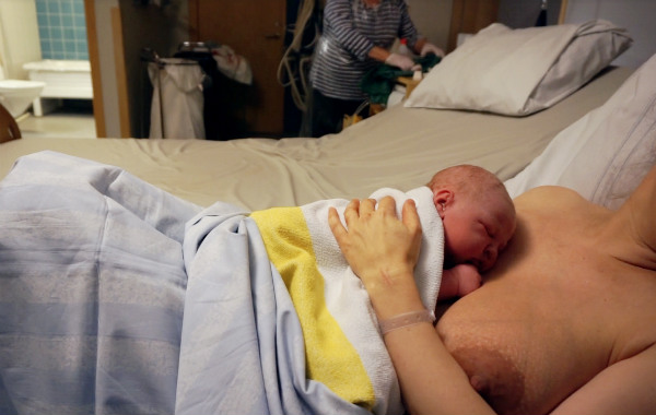 när du snart ska börja amma. Nyfödd bebis på BB, ligger på mammans bröst. Barnmorska i bakgrunden.