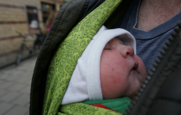 När du snart ska börja amma. Nyfödd bebis bärs på pappas bröst i grön bärsjal, utomhus.