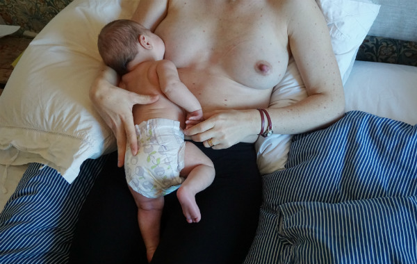 Tillbakalutad amning, laid back, bebis ligger mage mot mage med sin mamma och ammar, i säng.