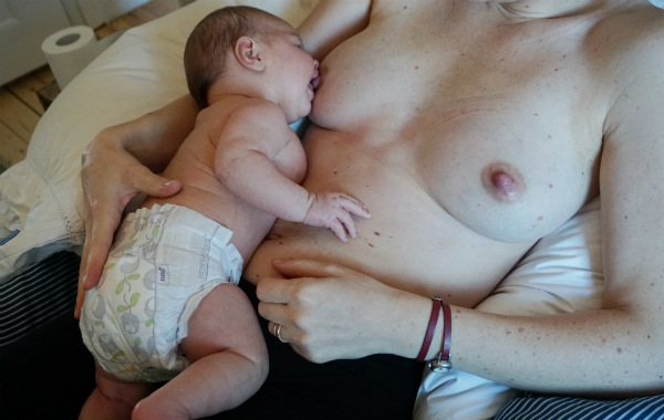 Tillbakalutad amning, laid back, barnet tar bröstet på mammans mage, på säng.