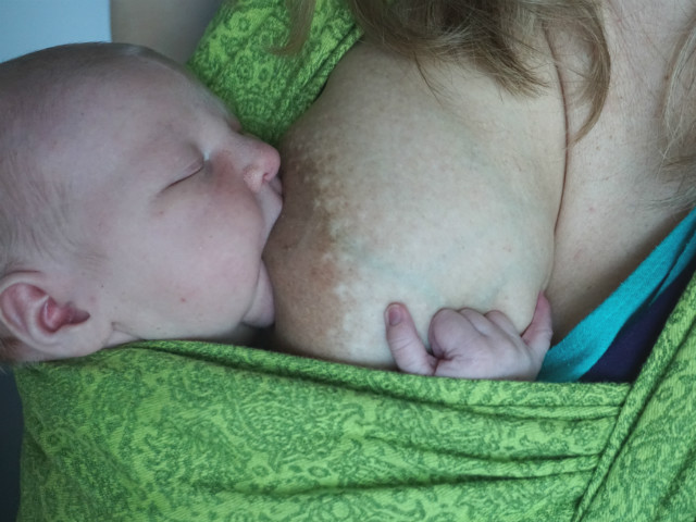 Tilläggsmata mindre, ge mindre ersättning. Fem dagar gammal bebis ammar upprätt sittande i grön bärsjal.