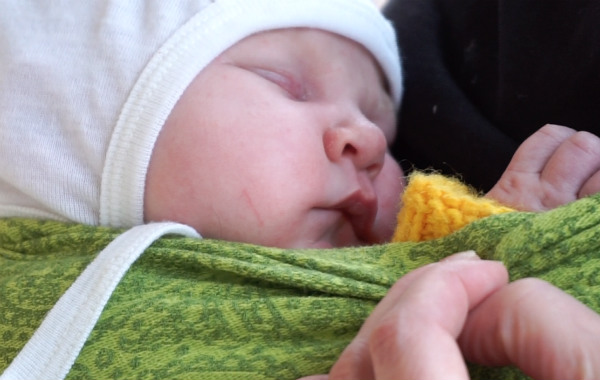 Amningsdagbok del tre. Nyfödd bebis har somnat i grön bärsjal, utomhus.