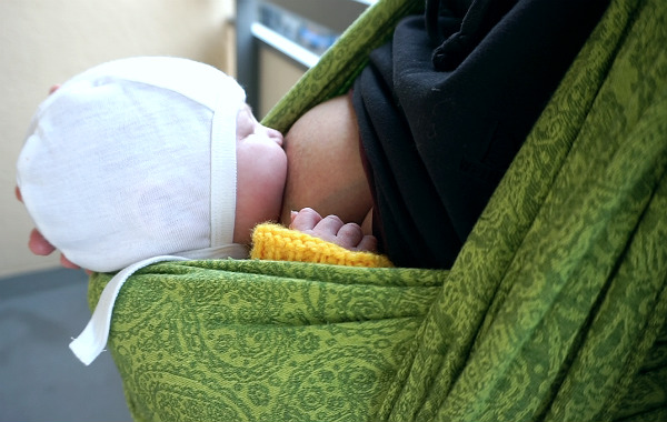 Amningsdagbok del tre. Nyfödd bebis ammar upprätt sittande i grön bärsjal, utomhus.