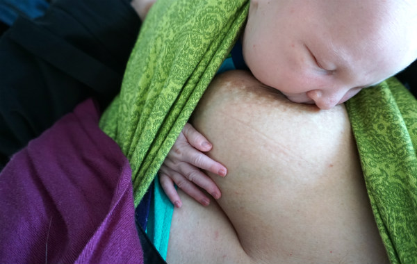 Amningsdagbok del två. Nyfödd bebis ammar i grön bärsjal, upprätt sittande.