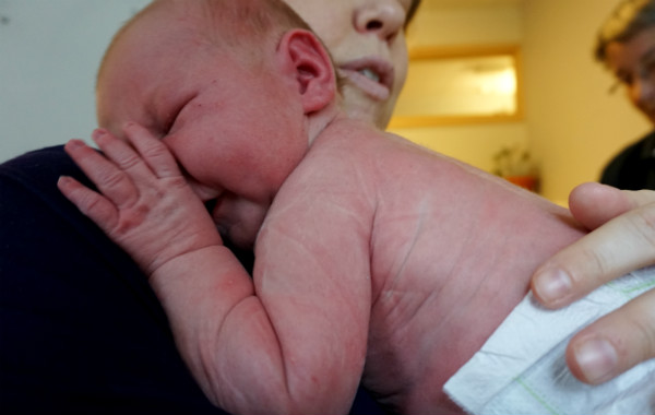 Amningsvänlig tilläggsmatning. Nyfödd bebis vilar mot mammans axel på BB.