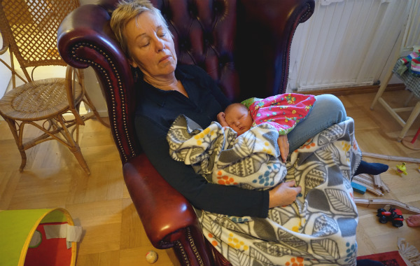 Amningsdagbok del tre. Nyfödd bebis sover i famnen på sin mormor, som slumrar i fåtölj.