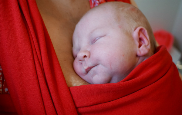 Amningsdagbok del fyra. Bebis sover i röd bärsjal.