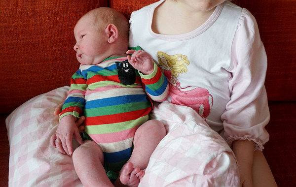 Amningsdagbok del tre. Nyfödd bebis i famnen på storasyster, i soffa.