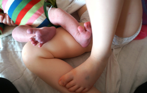 Amningsdagbok del tre. Nyfödd bebis ben plus större syskons ben, de ligger på säng.