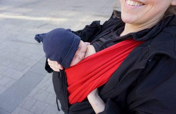 Tips om hur du ammar i bärsele och bärsjal. Liten bebis ammar i röd bärsjal utomhus.
