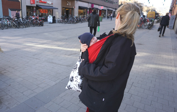 Tips om hur du ammar i bärsele och bärsjal. Liten bebis ammar i röd bärsjal utomhus, gatumiljö.