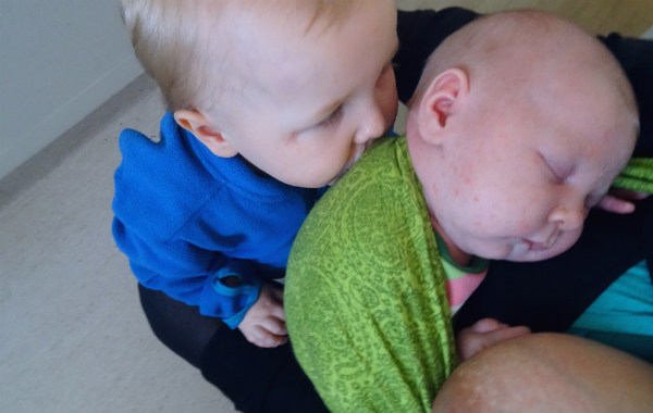 Amningsdagbok del tre. Nyfödd sovande bebis i grön bärsjal får puss av storebror.