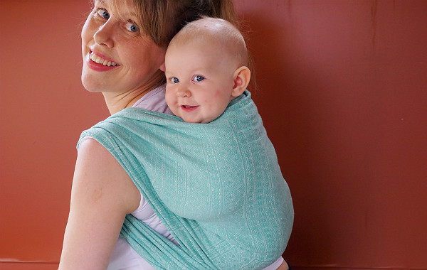 Bära barn på ryggen. Glad bebis i bärsjal på mammas rygg.