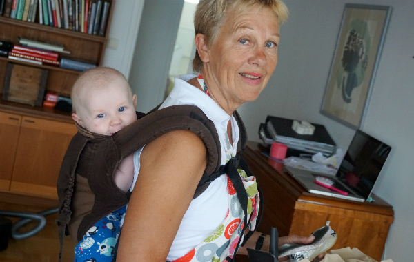 Bära barn på ryggen. Mormor bär bebis i bärsele på ryggen, vardagsrum.
