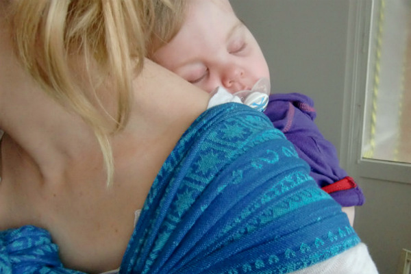 Bära barn på ryggen, bebis har somnat på mammas rygg i bärsjal, suger på napp.