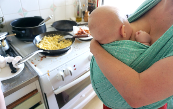 Tips om hur du ammar i bärsele och bärsjal. Barn ammar i bärsjal i kök medan mamman steker ägg.