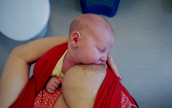 Tilläggsmata mindre, ge mindre ersättning. Amning på toa. Nyfödd bebis ammar i röd bärsjal, upprätt sittande.