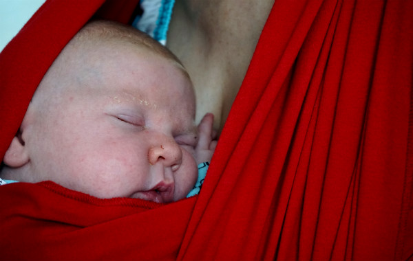 Amningsstrejk. Bebis sover i röd bärsjal.