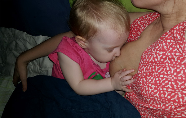 Amning och ont i ryggen. Ettåring ammar i säng på sin mammas arm.