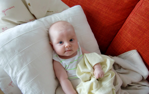 Mest förvirrande sakerna med amning. Bebis vilar mot kudde i soffa.