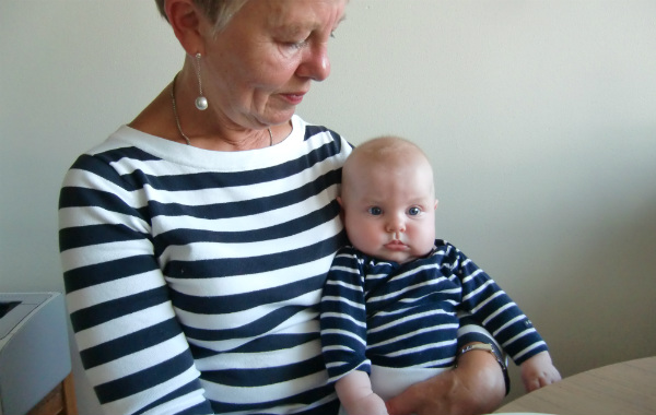 Mest förvirrande sakerna med amning. Mormor med liten bebis vid köksbord, båda i randiga tröjor.