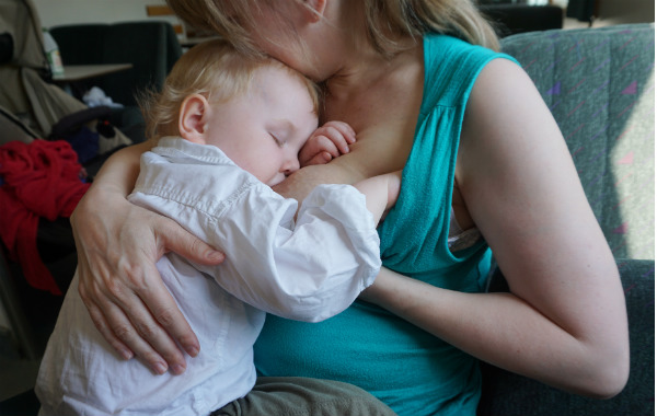 Tvååring sitter och ammar i mammans famn.